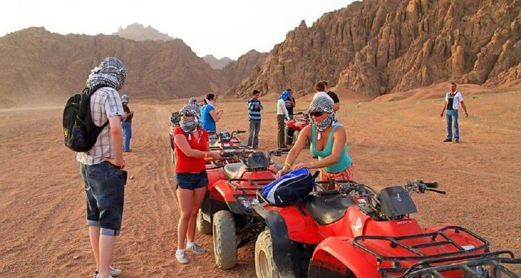 Group of people preparing ATV rides in a desert landscape.