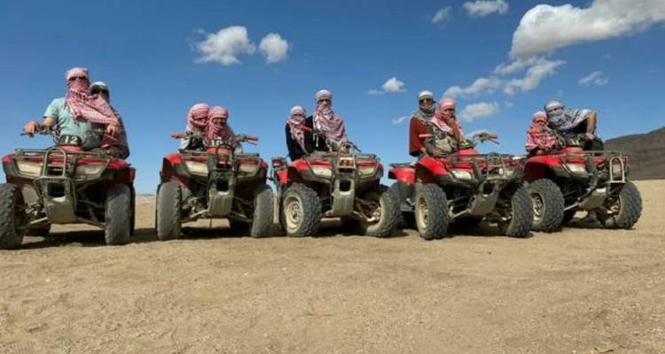 Several people posing on ATVs in a barren landscape.