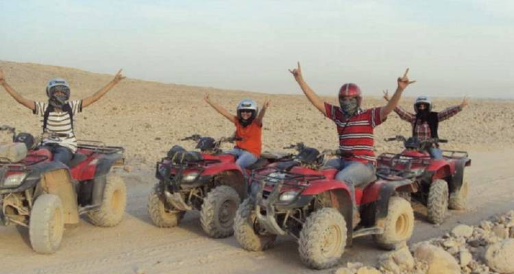 Group of individuals raising arms excitedly on ATVs in a desert.