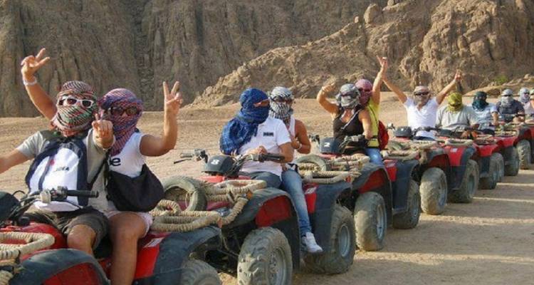 Line of people riding ATVs amidst rocky desert formations.