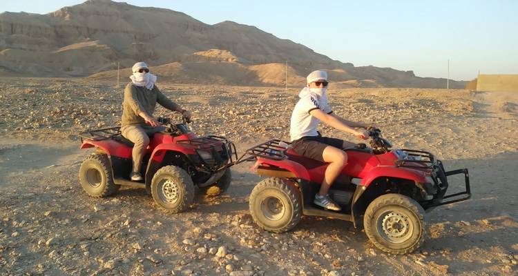 Two people on ATVs with a background of rocky terrain.