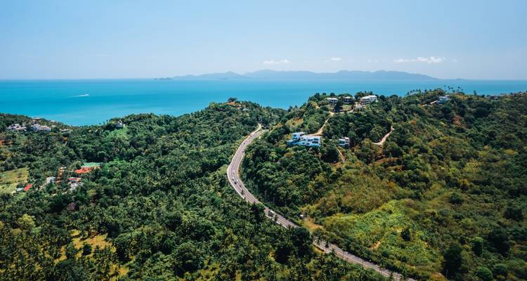 Paysage vallonné avec une route sinueuse et vue sur l'océan.