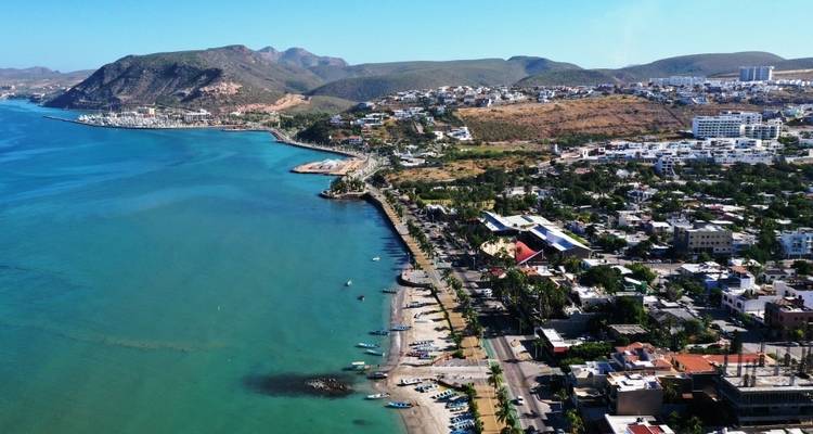Eine Luftaufnahme einer Küstenstadt mit einem langen Strandabschnitt und Bergen im Hintergrund.