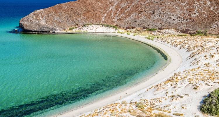 Ein einsamer Strand mit klarem Wasser und felsigen Hügeln, die ihn umgeben.