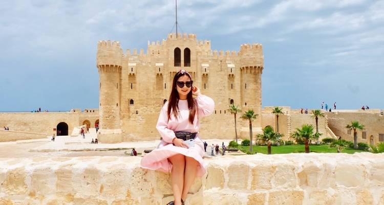 Femme assise sur un mur de forteresse avec un fort en arrière-plan.