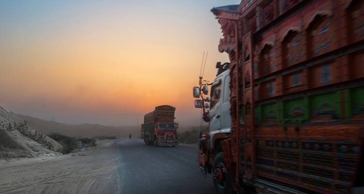 Bunte Lastwagen fahren bei Sonnenuntergang auf einer Landstraße.