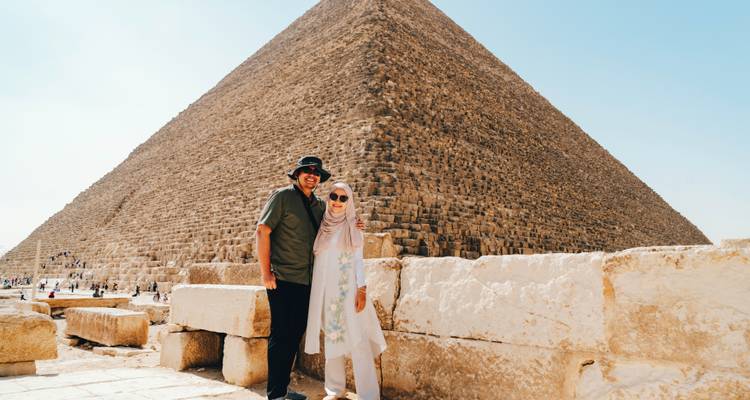 Een stel dat poseert voor een grote piramide in fel zonlicht.