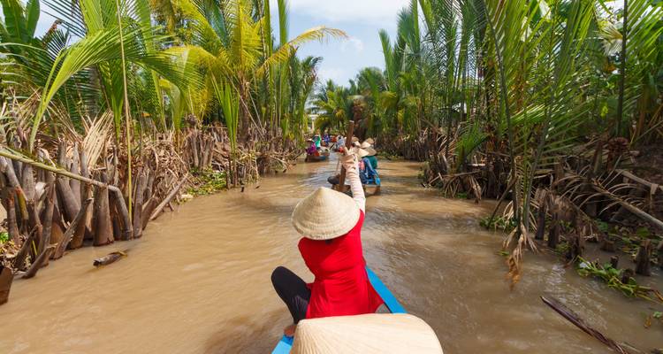 Touristen, die in kleinen Booten durch eine üppige Wasserstraße paddeln.
