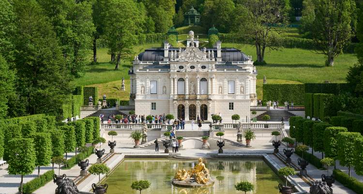 Ornate Linderhof Palace reflected in a fountain pool surrounded by manicured Baroque gardens.