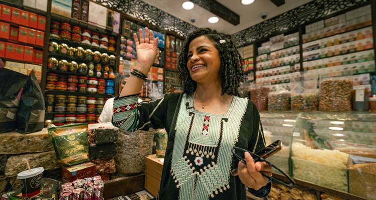 Femme qui fait signe à l'intérieur d'une boutique de marché colorée.