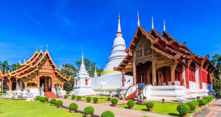 Traditionelle Tempelgebäude mit weißer Stupa und gepflegtem Garten.