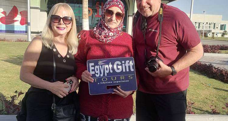 Drei Personen posieren mit einem Schild vor einem modernen Gebäude.