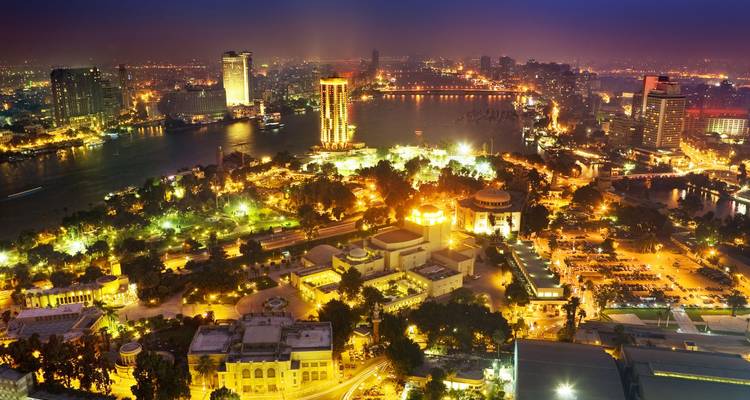 Vue aérienne nocturne de la ligne d'horizon du Caire avec les ponts illuminés et les bâtiments se reflétant sur le Nil.