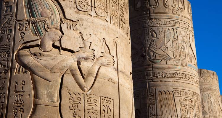Des hiéroglyphes complexes gravés dans d'énormes colonnes de grès qui brillent sous un ciel bleu dégagé.