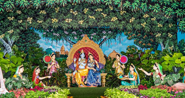 Un diorama vívido que muestra a Krishna y Radha rodeados de asistentes en una exuberante escena de jardín pintado.