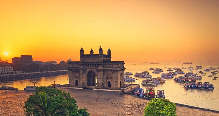 Gateway of India silhouetted against an orange sunrise with a harbor full of boats in Mumbai.