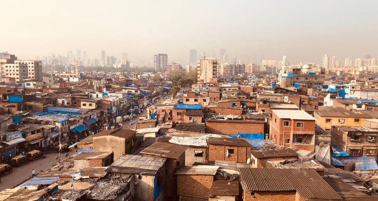 Expansive view over dense low-rise housing and slums of Mumbai under a hazy sky.