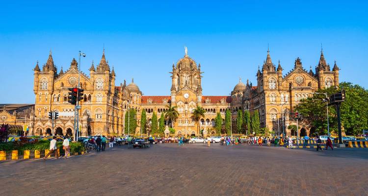 The Gothic Revival façade of Chhatrapati Shivaji Terminus dominates a bustling urban square filled with traffic and pedestrians.
