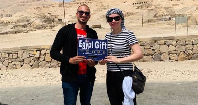 El guía y el viajero sostienen un cartel de 'Egypt Gift Tours' en el paisaje desértico cerca de los acantilados antiguos de Luxor.