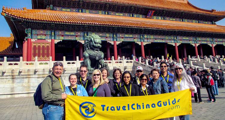 Un grupo de turismo alegre posa con un banner brillante antes de los salones ornados de la Ciudad Prohibida de Beijing.
