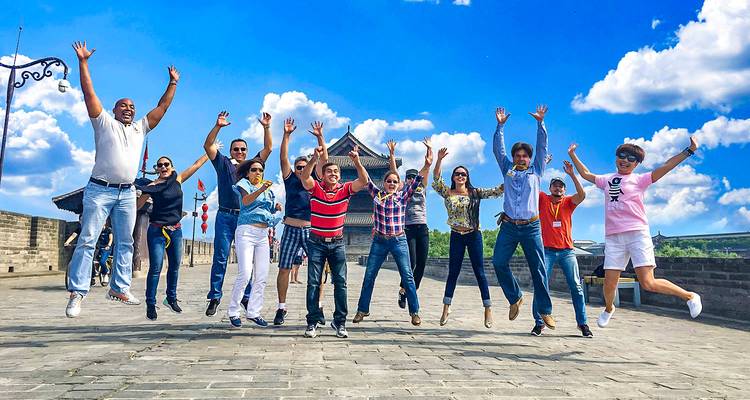 Un grupo grande salta alegremente contra un cielo azul brillante en una muralla de una ciudad antigua.