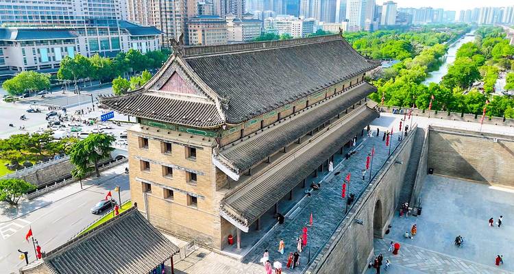 Vista aérea de la torre de vigilancia de la muralla antigua de Xi'an con el paisaje urbano moderno y el foso arbolado debajo.