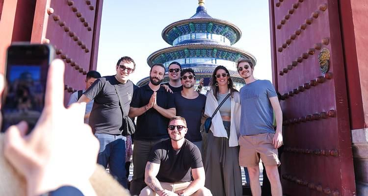 Amigos sonrientes posan entre las puertas rojas abiertas del palacio que enmarcan el Templo del Cielo de Beijing de fondo.