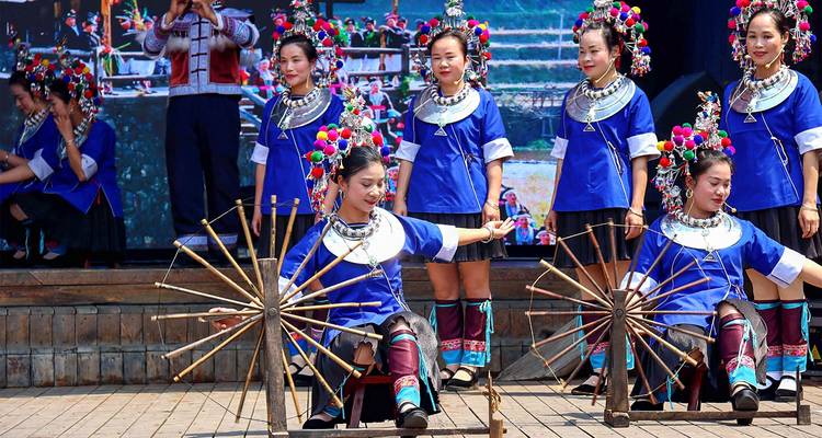 Bailarines de minorías étnicas coloridos con túnicas azules realizan una rutina tradicional de rueda giratoria en un escenario al aire libre.