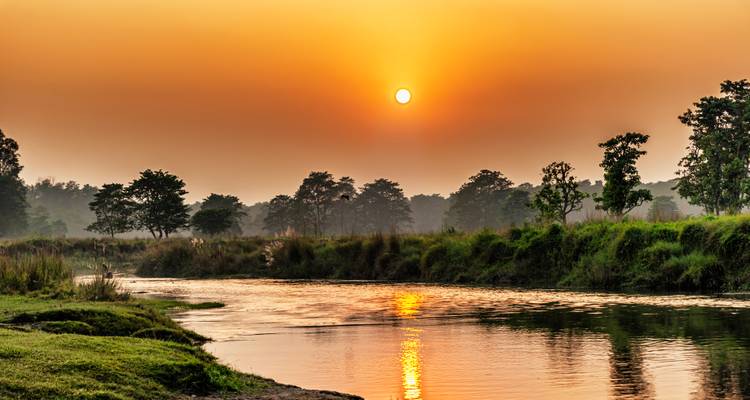 Un sol de naranja quemado cayendo sobre un tranquilo río de la selva en el Parque Nacional de Chitwan.