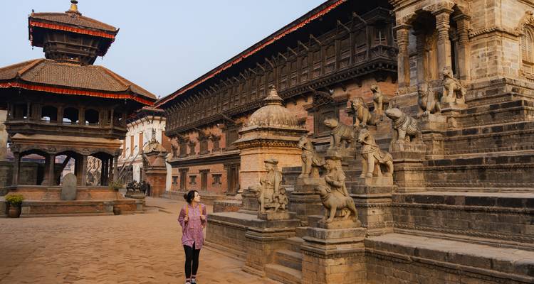 Een vrouw die door een historische binnenplaats loopt met traditionele Nepalese architectuur.