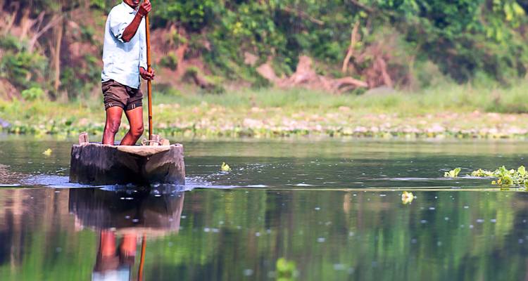 Un homme pagayant en canoë sur une rivière entourée de verdure.