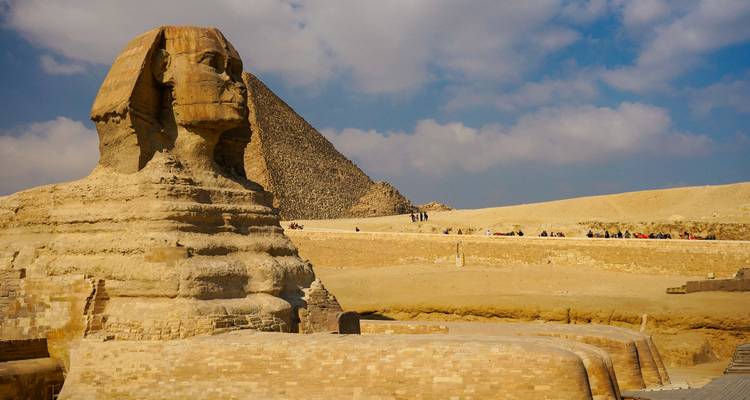 The Sphinx with a pyramid in the background under a blue sky.