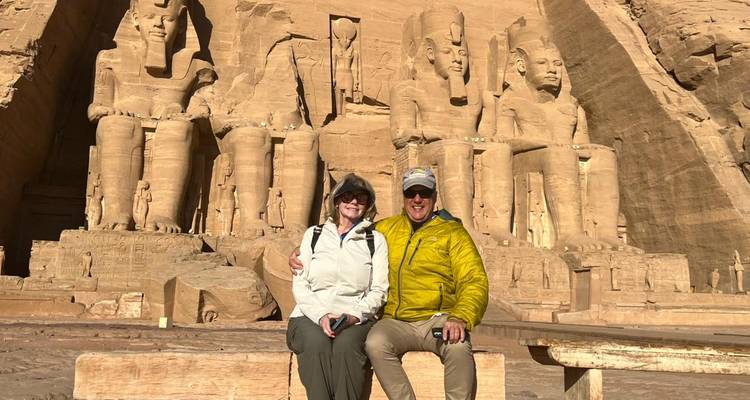 Pareja mayor sentada en banco sonriendo con la fachada del templo de Abu Simbel elevándose detrás.