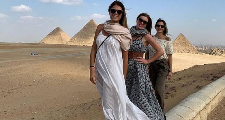 Tres mujeres posan con estilo frente a las pirámides en una tarde brillante del desierto.