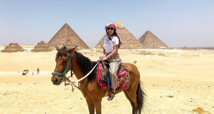 Viajero a caballo posa ante las pirámides bajo un cielo azul despejado del desierto.