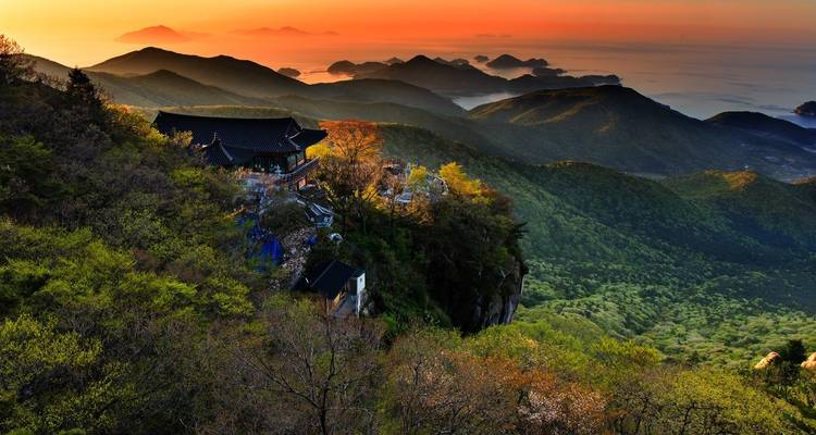 Zonsondergangzicht over heuvels met een traditionele Koreaanse tempel.