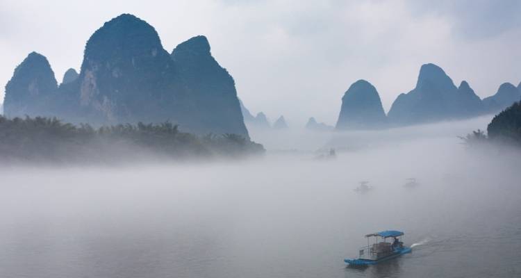 Paisaje kárstico brumoso con barcos en un río.