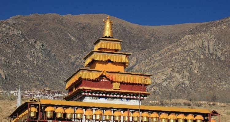 Eine goldbekrönte Stupa vor einer bergigen Kulisse.