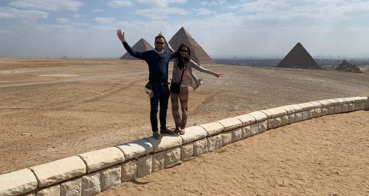 Couple posant avec les bras levés devant les pyramides de Gizeh.
