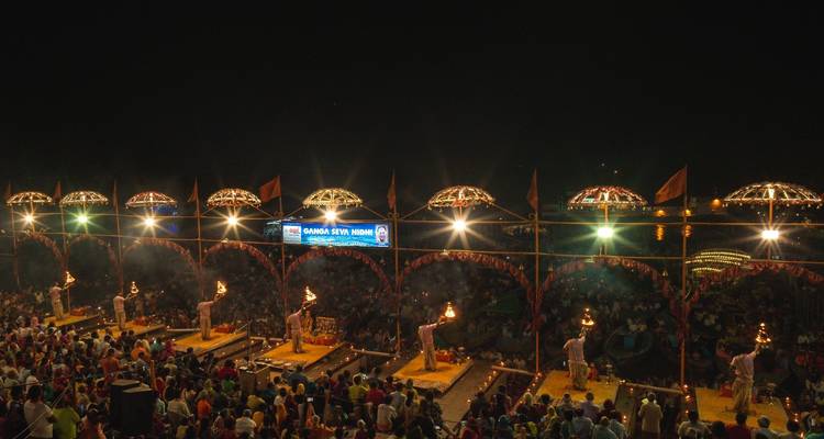 Cérémonie nocturne en bord de rivière avec des prêtres accomplissant des rituels d'aarti sur des plates-formes surélevées devant une foule nombreuse.