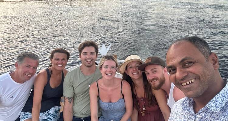 Groep mensen die glimlachen op een boot met water op de achtergrond.