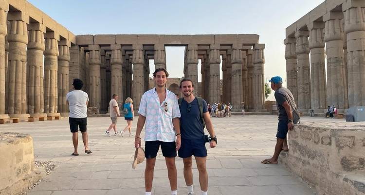 Twee mannen die voor indrukwekkende oude zuilen staan.