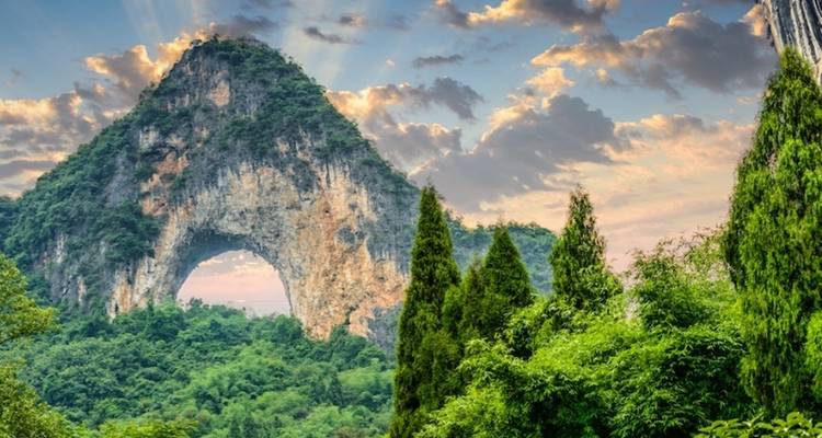 A mountainous landscape with a natural arch, surrounded by lush greenery.