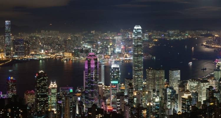 Nighttime panoramic view of a city skyline with skyscrapers and a harbor.