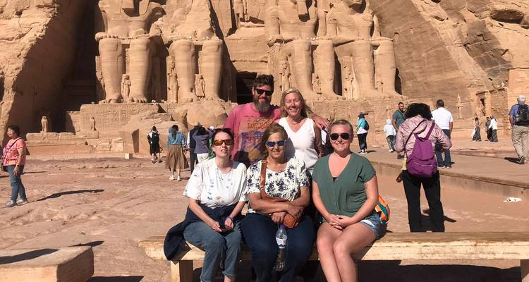 Tourists seated on a bench with the colossal statues of Abu Simbel towering behind.