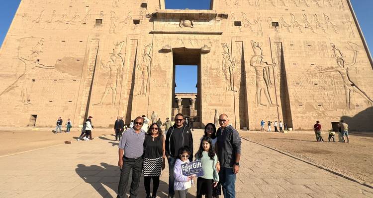 Family holding a sign in front of the massive sandstone pylon of Edfu Temple.