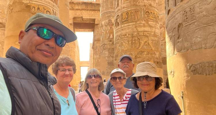 Older travelers gathered inside a hypostyle hall with vividly carved and painted columns.