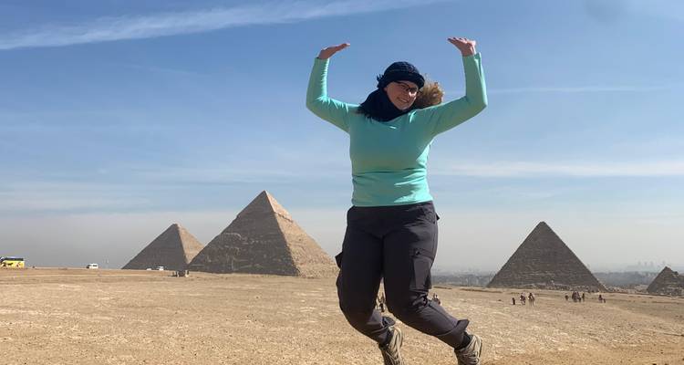 Traveler mid-jump with outstretched arms before the three pyramids on a clear day.