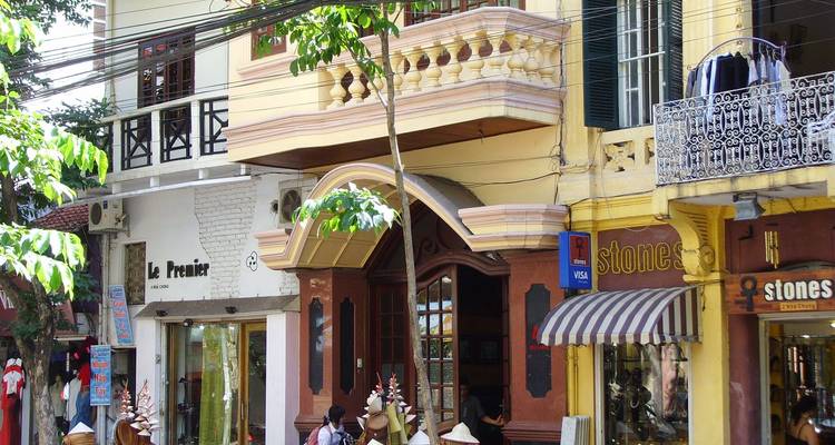 Colorful colonial-era shopfronts with balconies and signs along a leafy street