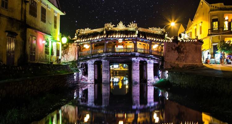 Beleuchtete Brücke über einem Fluss bei Nacht, mit reflektierender Beleuchtung.